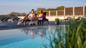 2 vrouwen op een ligstoel naast het buitenzwembad van Fletcher Wellness-Hotel Helmond